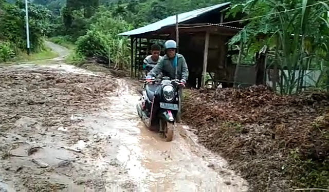 Warga sedang melintasi jalan yang longsor.